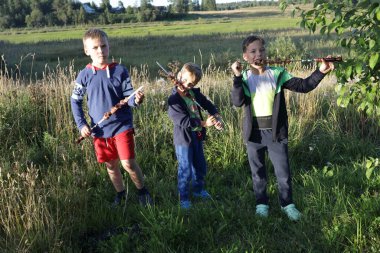 Üç çocuk çimenlikte şiş kebap yiyor.