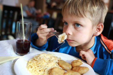 Restoranda spagettiyle nugget yiyen çocuk.