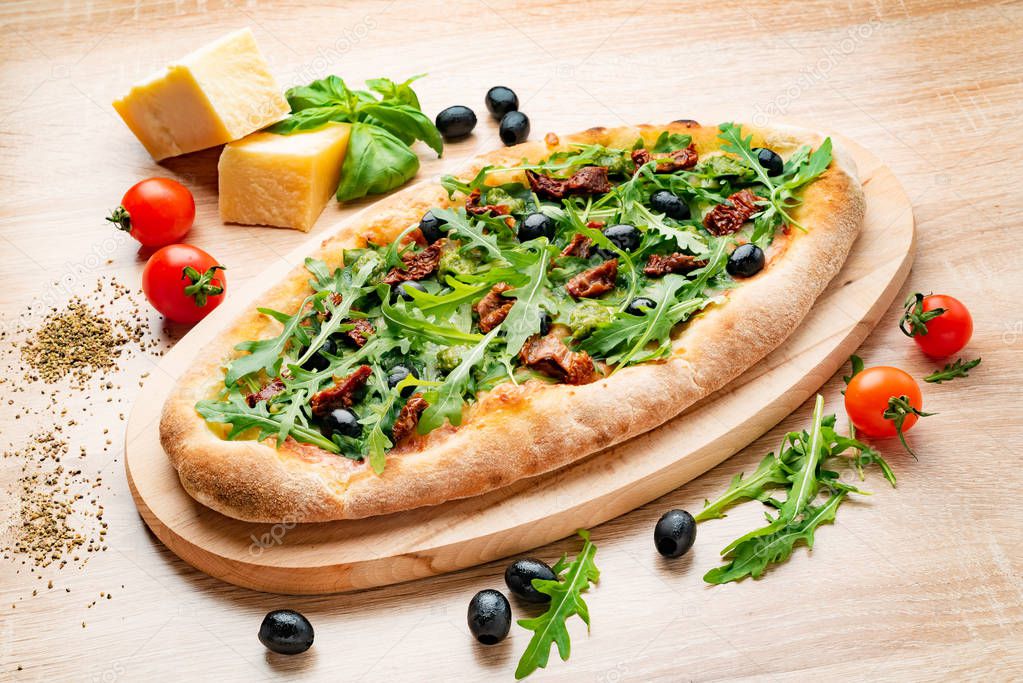 Flatbread pizza garnished with fresh arugula on wooden pizza board