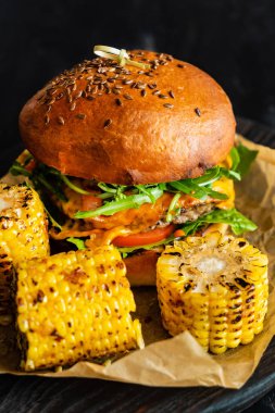 Delicious cheeseburger with corn on the black pan clipart