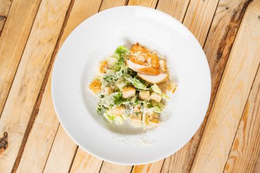 Beyaz tabakta taze sezar salatası, ahşap arka plan.