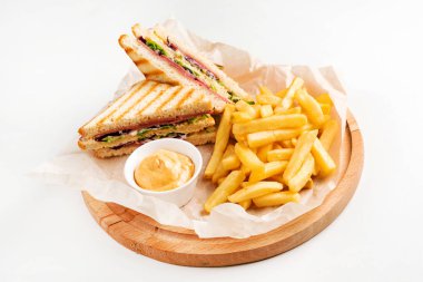 Peynirli klüp sandviç, turşulu kraker, domates ve füme et. Patates kızartmasıyla süslenmiş.