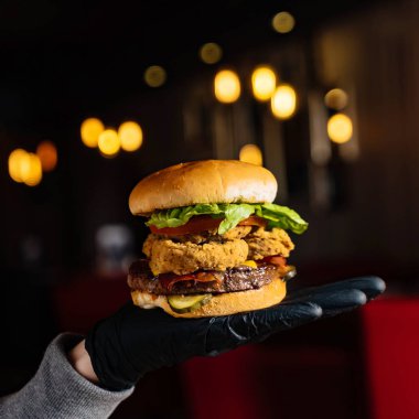 Siyah eldivenli bir adam restoranda hamburger yiyor.