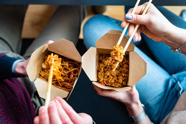 couple eating food packed in take-away box with chopsticks