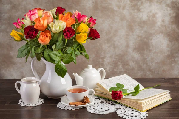 Still life roses, tea and a book on the table.