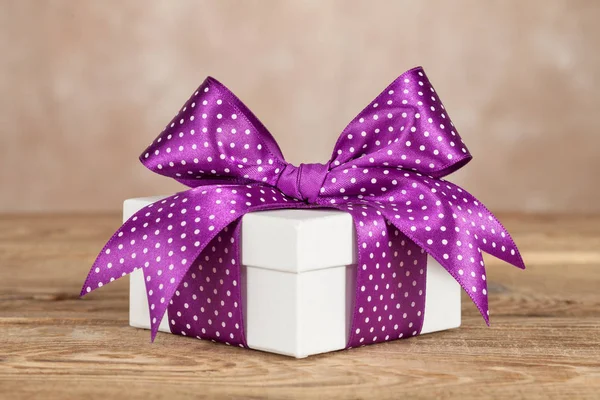 White gift box with a violet bow on the old board. — Stock Photo, Image