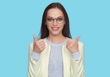 Güzel kız yukarı başparmak ile fotoğraf makinesinde gülümseyen fotoğrafını. Güzel kadın gözlük takıyor. mavi arka plan üzerinde izole