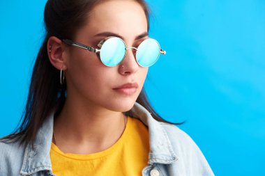 Genç kadın modern bir güneş gözlüğü takıyor. Parlak mavi bir arka plan üzerinde izole