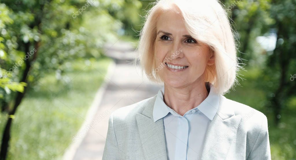 Happy blonde mature woman outdoors portrait. Middle aged lady smiling and daydreaming.