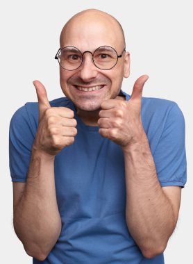 Gözlük ve başparmak tabela yapım ve neşeyle gülümseyen t-shirt giyen mutlu orta yaşlı beyaz kel adam