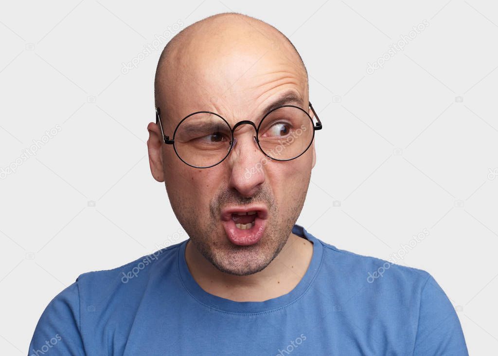 Portrait of man with silly grimace isolated over gray background. Bald guy looking with disgust at somebody