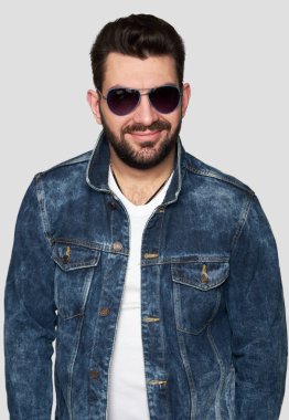 yakışıklı kendini beğenmiş güneş gözlüğü ve trendy denim ceket giyen adam sakallı. Gri arka plan üzerinde izole