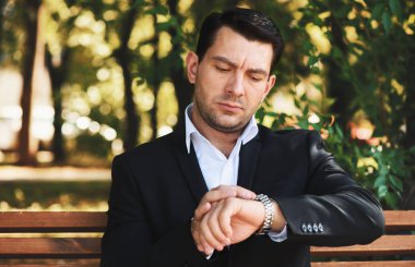 Onun gözetiminde görünen ciddi adam. Parkta bir bankta oturmuş elbiseli yakışıklı adam