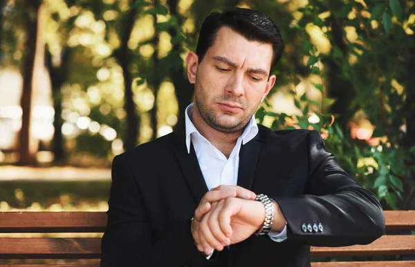 Onun gözetiminde görünen ciddi adam. Parkta bir bankta oturmuş elbiseli yakışıklı adam