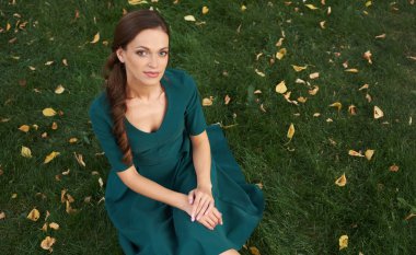 yeşil çimenlerin üzerinde oturan bir elbiseli güzel kadın. Açık portre