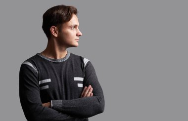 Profil sahibi emin yakışıklı bir adam. Kollarını çapraz ile genç adam uzakta arıyor. Gri studio arka plan üzerinde izole