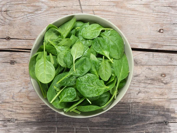Fresh spinach leaves in bowl on rustic wooden table — Stock Photo, Image