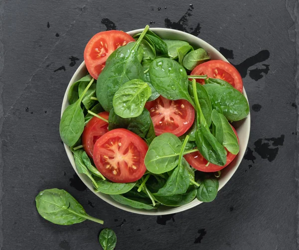 Ensalada de espinacas y tomate en un tazón sobre tabla de piedra gris. Vista superior —  Fotos de Stock