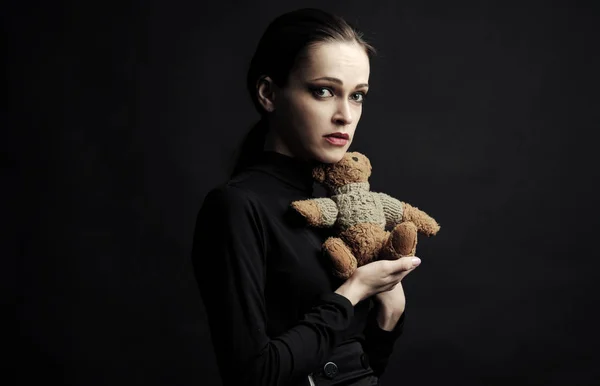 Traurige Frau hält Teddybär-Spielzeug über schwarzem Studiohintergrund — Stockfoto