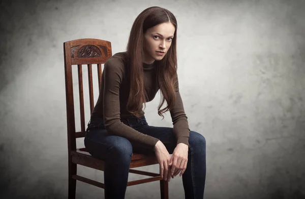 Pretty brunette woman is sitting on a chair in studio — Stock Photo, Image