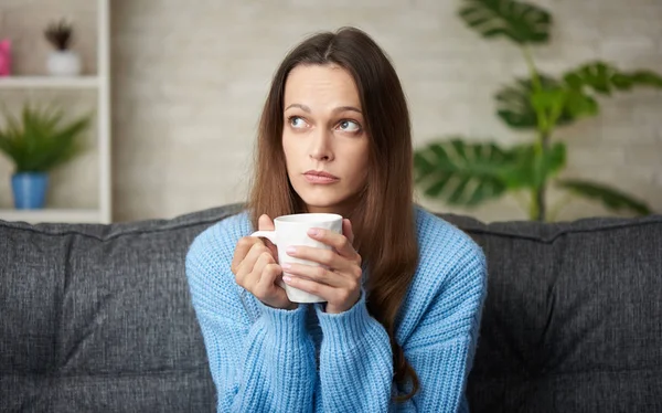 Sad woman sitting on a sofa in the living room — Stock Photo, Image