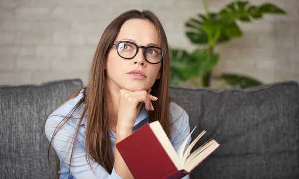 Bekymmerslös vacker kvinna läser en bok medan du sitter på en så — Stockfoto