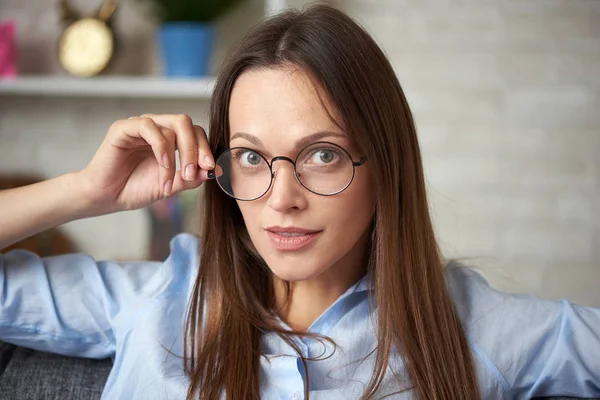 Mujer joven en gafas está sentado en un sofá — Foto de Stock