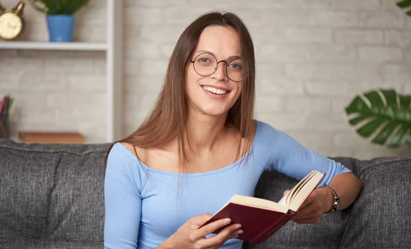 Pretty ung kvinna i glasögon läser en bok hemma — Stockfoto