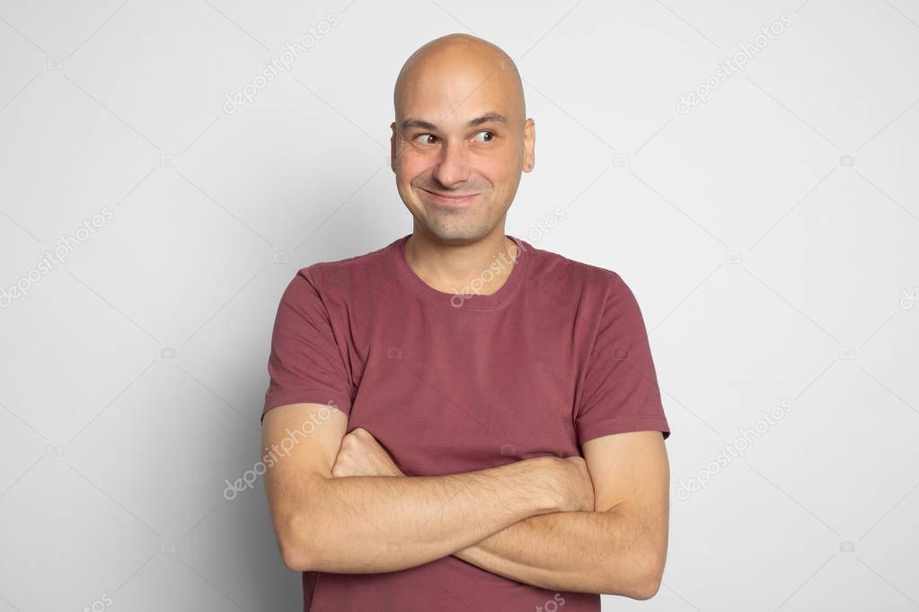 Cheerful bald man is looking away with tricky smile on his face