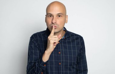 40 yaşında kel bir adam işaret parmağını dudaklarında tutuyor.