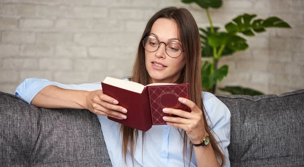 En vacker kvinna läser en bok hemma. — Stockfoto