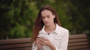 Mutlu kadın cep telefonuyla konuşmaktan zevk alıyor. Parktaki bankta otururken telefonda iyi haberler okuyan neşeli kızı kapat.