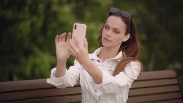 きれいな女性が公園のスマートフォンで自撮りしています 夏の日 屋外肖像画 — ストック動画