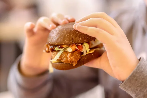 Burger in the hands of a teenager. Fast food in the mall.