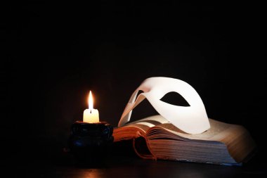 Koyu arka plan aydınlatma mum yakınındaki eski kitap klasik beyaz Venedik Maske