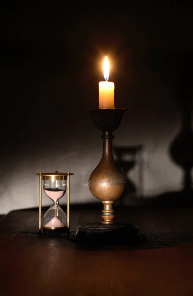 暗い背景に砂時計の近くの照明ろうそくとエレガントな真鍮製の燭台 — ストック写真
