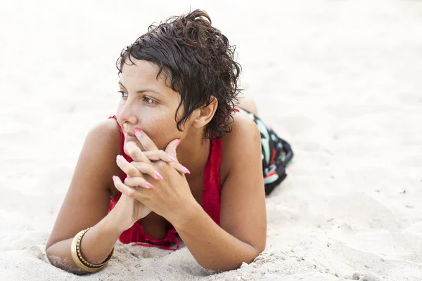 Attractive brunet woman in red lying on a sand. — Stock Photo, Image