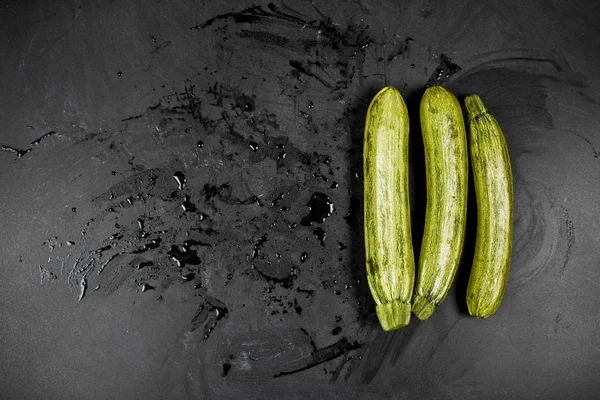 Courgettes fraîches humides vertes sur fond de tableau noir. — Photo