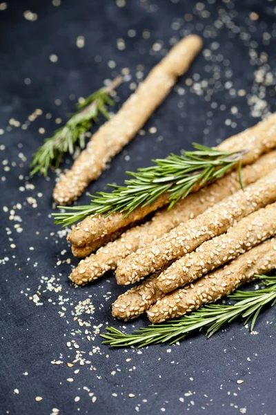 Italienska grissini bröd pinnar med sesam och rosmarin ört på b — Stockfoto