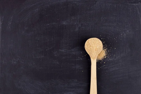 Azúcar de caña marrón en cuchara de madera sobre fondo negro . — Foto de Stock