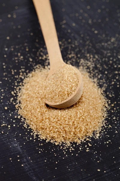 Azúcar de caña marrón en cuchara de madera sobre tabla negra . — Foto de Stock