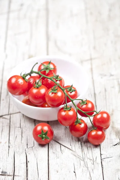 Fresh tomatoes in white bowl on rustic wooden table. — Stock Photo, Image