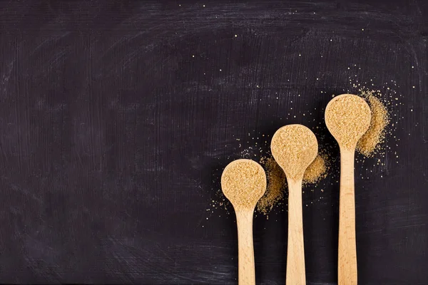 棕色甘蔗糖在三个木勺子在黑色背景. — 图库照片