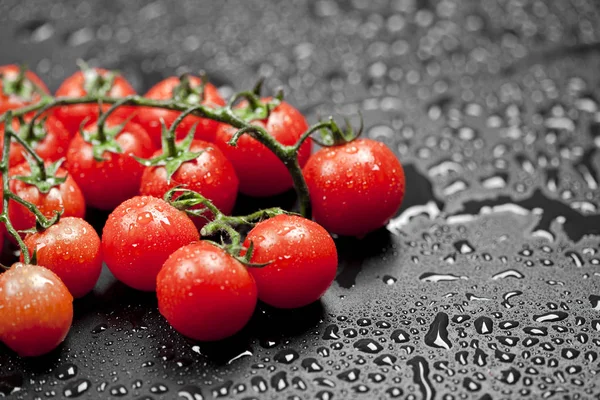 Tomates cereja orgânicos frescos bando closeup em preto molhado backgro — Fotografia de Stock