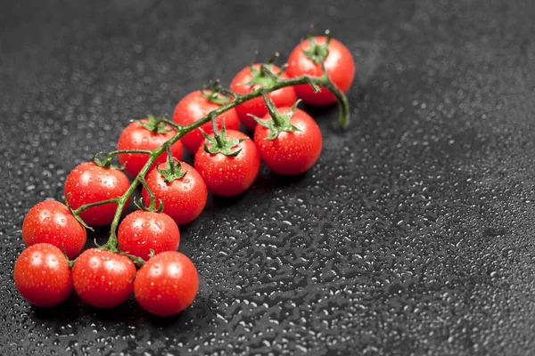 Свіжі органічні вишневі помідори крупним планом на чорному вологому фоні — стокове фото
