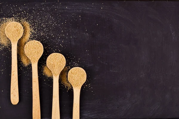 四个木勺与棕色甘蔗糖在黑色背景. — 图库照片