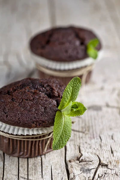 Muffins escuros de chocolate com folhas de hortelã closeup em madeira rústica — Fotografia de Stock