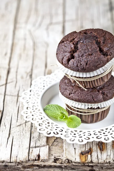 Dvě čerstvé tmavé muffiny s mátovou listou na bílém talíři — Stock fotografie