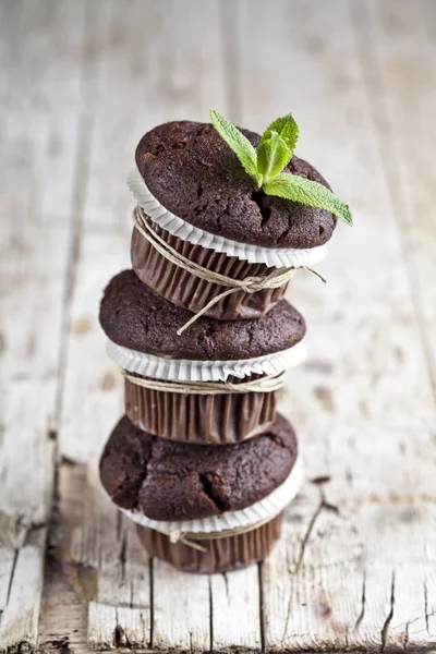 Três muffins de chocolate escuro frescos com folhas de hortelã em wo rústico — Fotografia de Stock