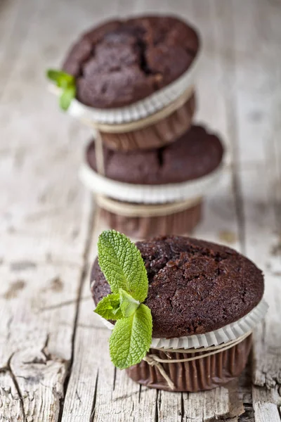 Três muffins de chocolate escuro frescos com folhas de hortelã em wo rústico — Fotografia de Stock